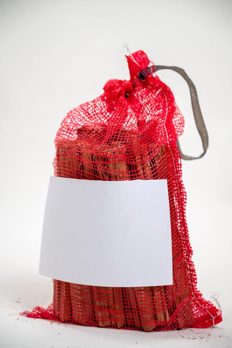 A bag of red sticks labeled "Firewood 24/7" on a white background, showcasing the blank side of the bag.