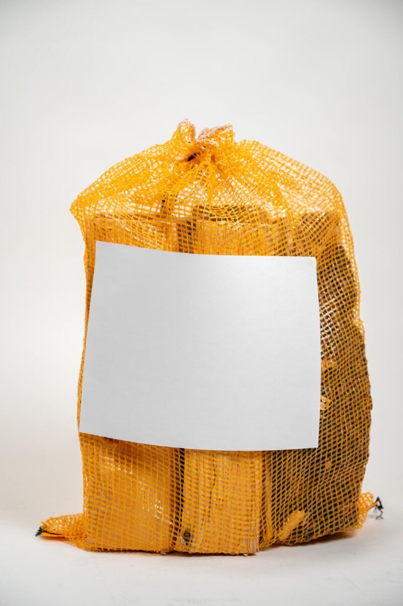 A yellow mesh bag containing several pieces of firewood, labeled "Firewood 24/7" with a blank label.