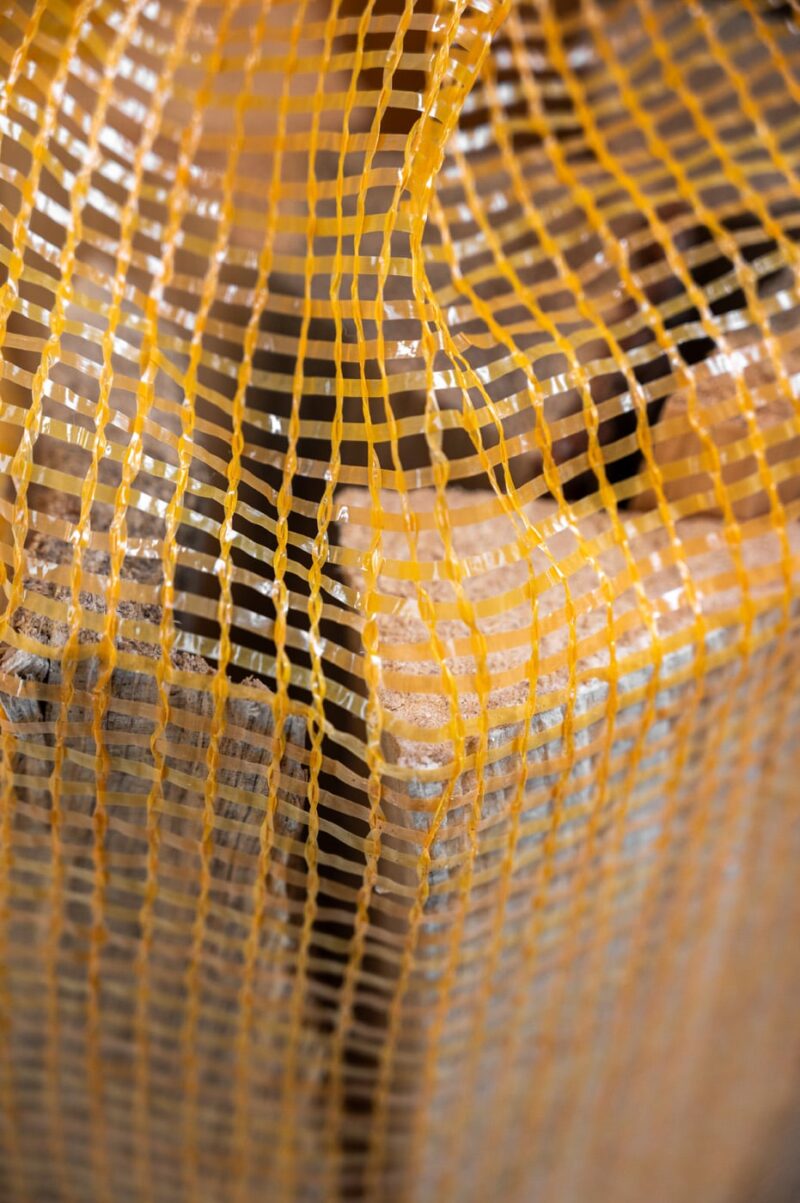 Close-up of a yellow mesh bag labeled "Firewood 24/7," showcasing its texture and design for wood storage.