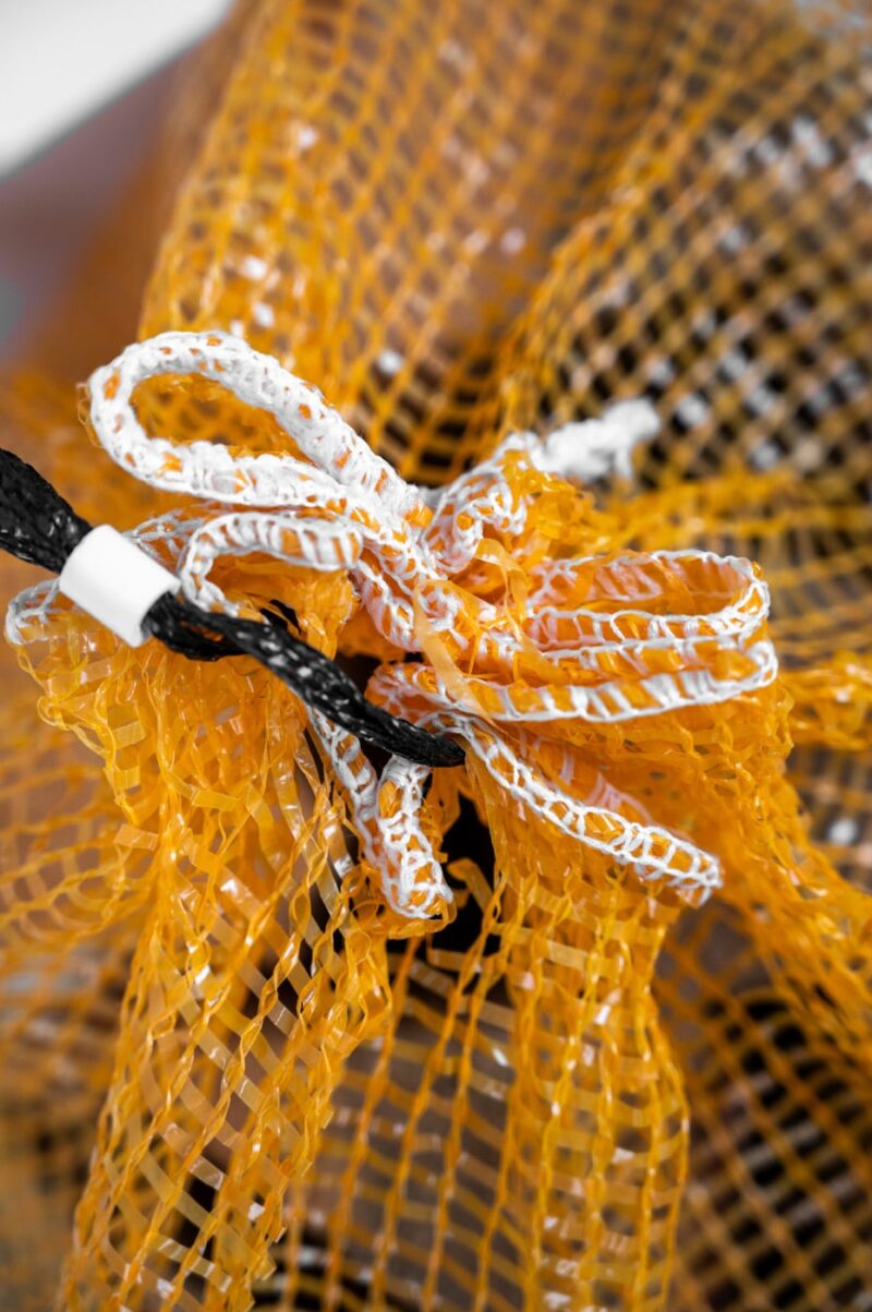 Close-up of a yellow bag tied with a string, labeled "Firewood 24/7," showcasing the seal view.