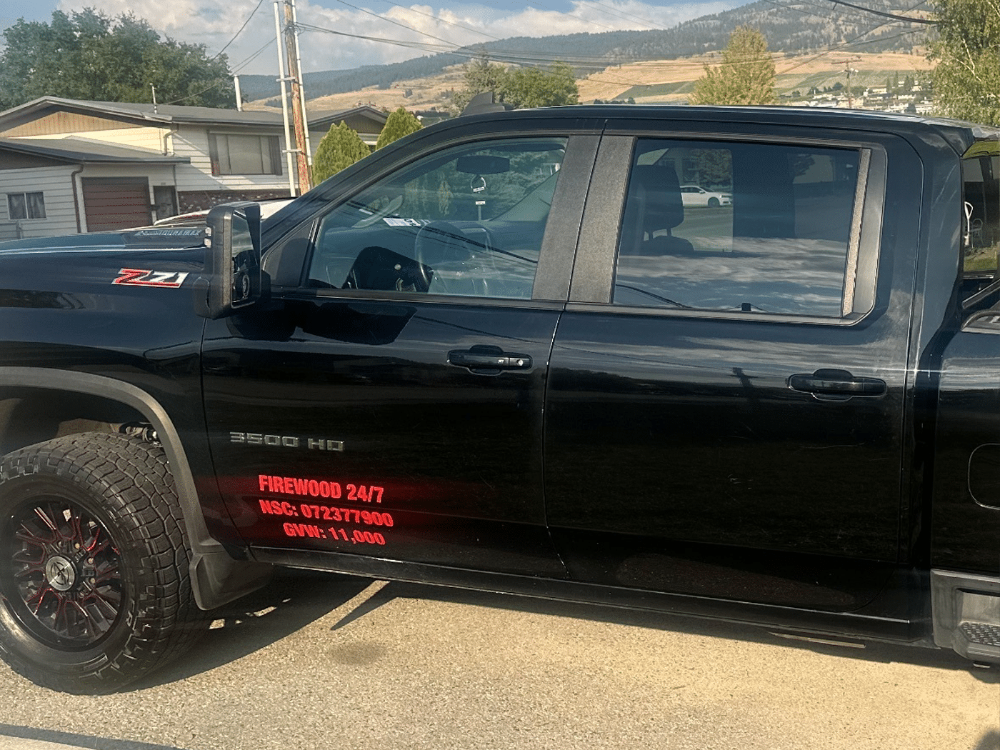 Black pickup truck parked with a sign reading "Firewood 24/7" displayed prominently on the side.